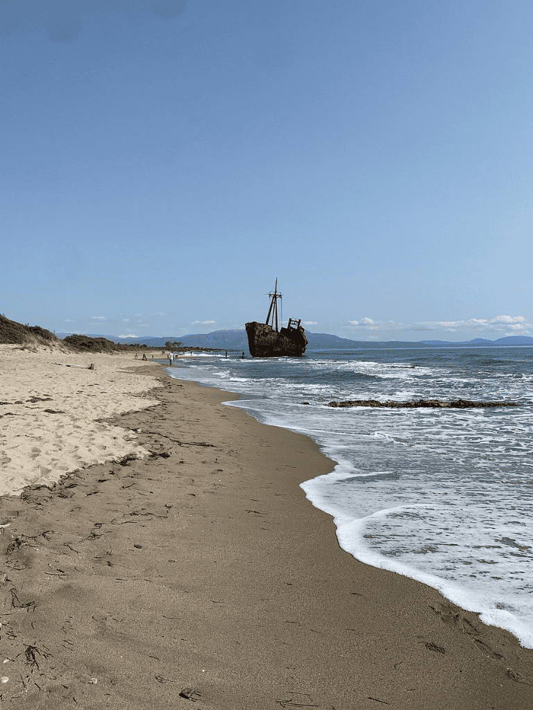 Abandoned shipwreck on the beach with ocean waves and sandy shore, scenic coastal landscape.