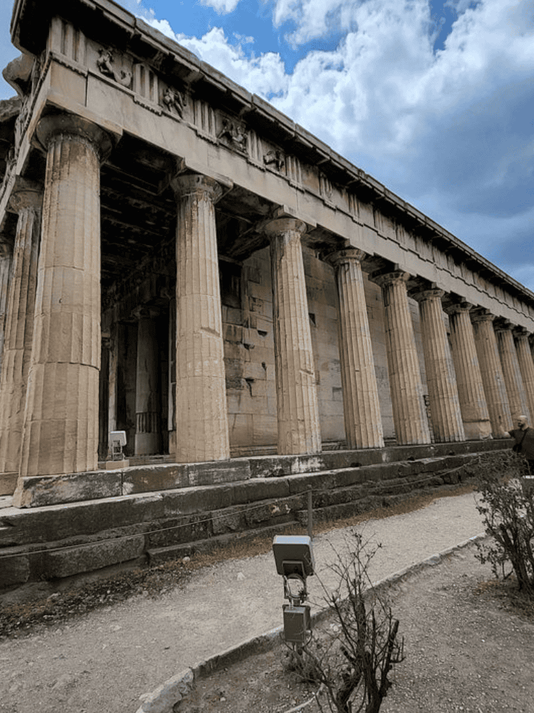 Ancient Greek temple with tall columns, historic ruins, clear sky, and clouds.