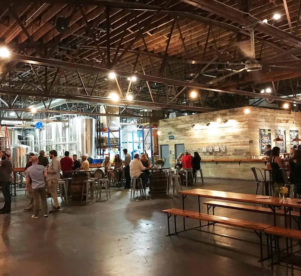 Modern brewery interior with brewing tanks, industrial design, and people enjoying craft beers.