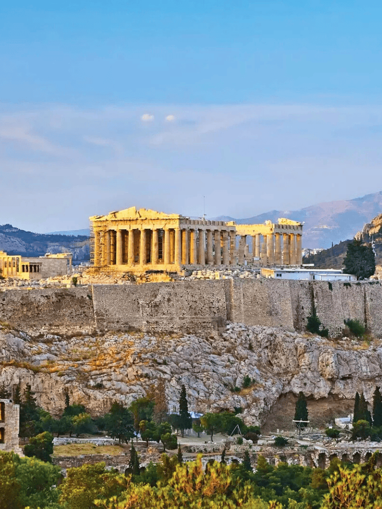 Ancient Greek Acropolis on the rocky hill, with blue sky and lush greenery in Athens, Greece.