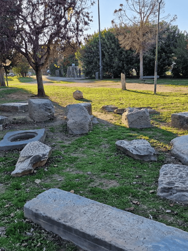 Large park rocks and trees in an open green space with a playground in the background.