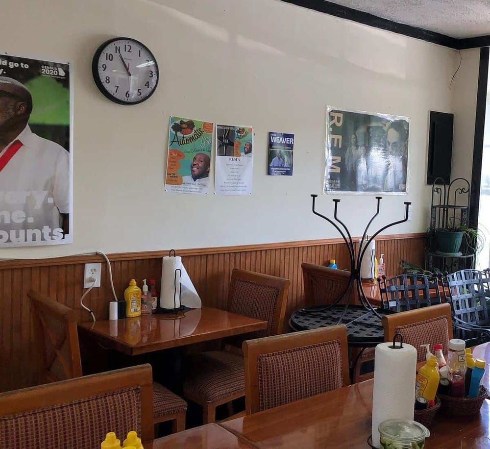 A cozy restaurant interior with wooden tables, chairs, wall decor, and condiments for customers.