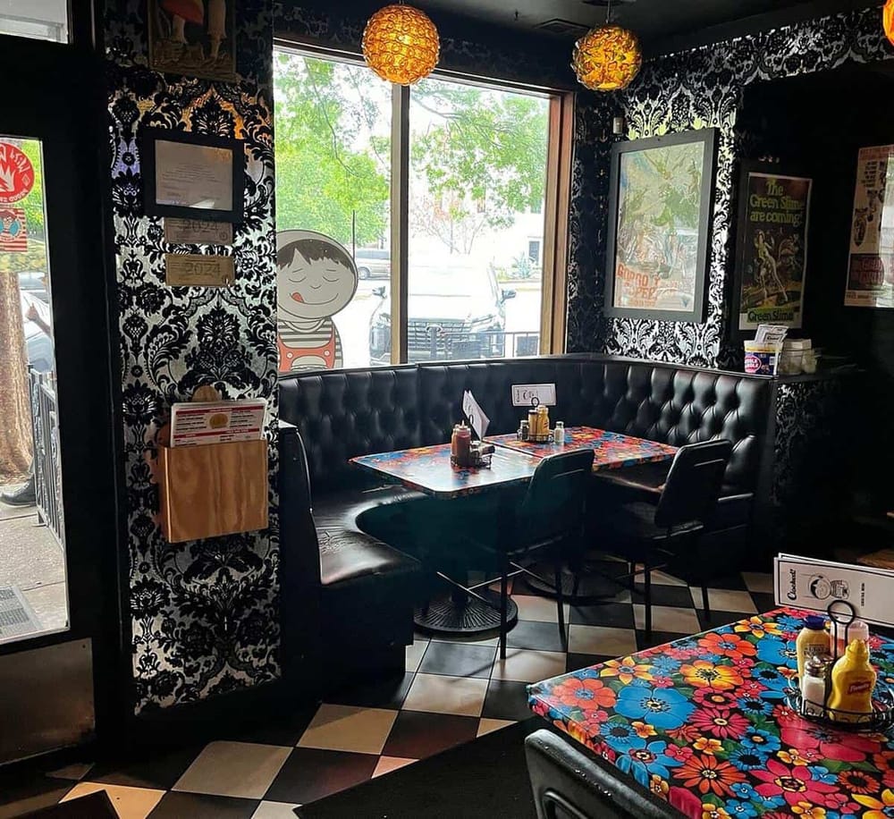 Cozy eclectic restaurant interior with colorful tables, black leather bench seating, and vintage decor accents.