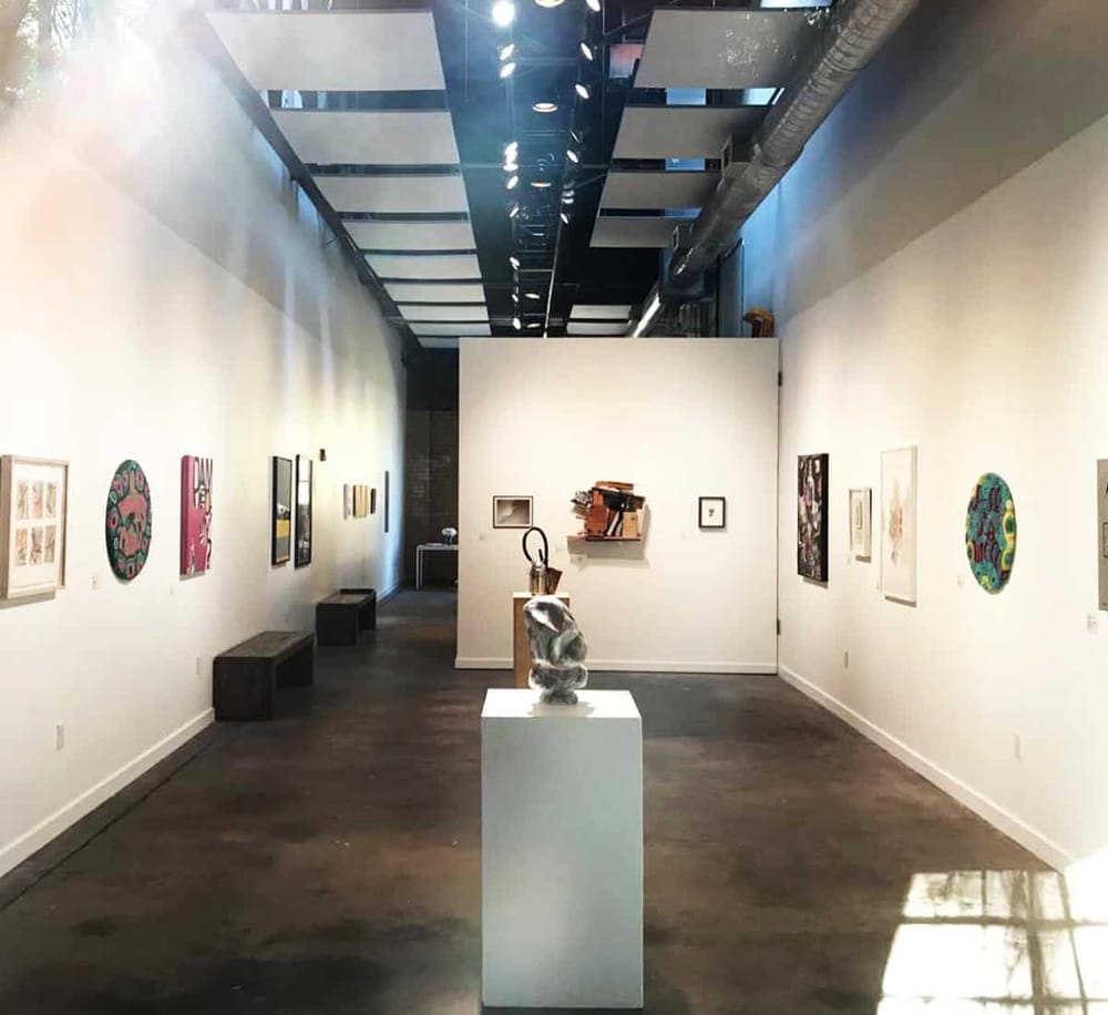 Colorful modern artwork displayed in an art gallery with white walls and dark flooring.