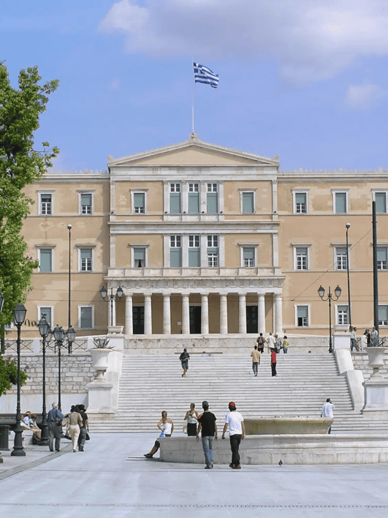 Greek Parliament building with visitors and flags.