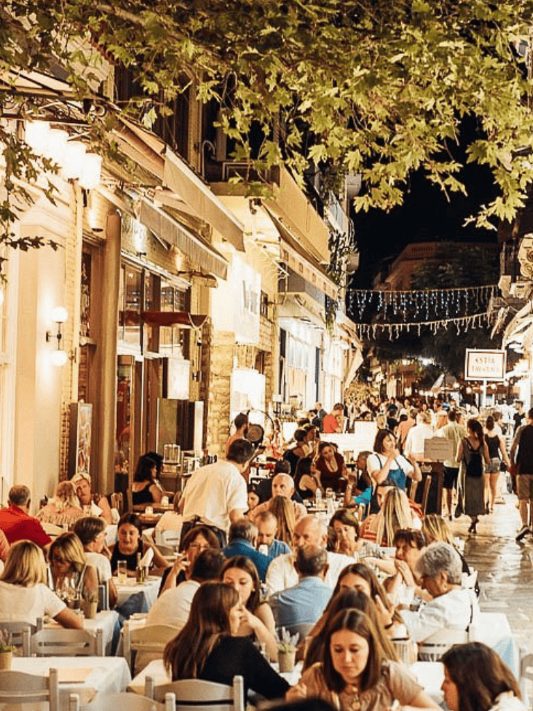 Vibrant outdoor dining street scene with crowded restaurants and festive string lights in a lively city atmosphere.