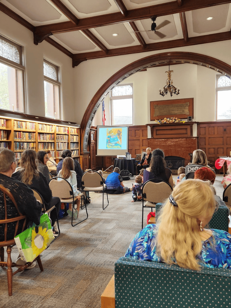 Meeting in a historic library for storytelling event with children and adults, warm wooden decor, large windows, and a fireplace.