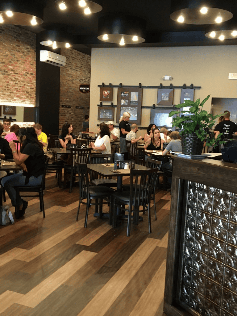 Cozy restaurant interior with guests dining, modern decor, and brick wall accents.