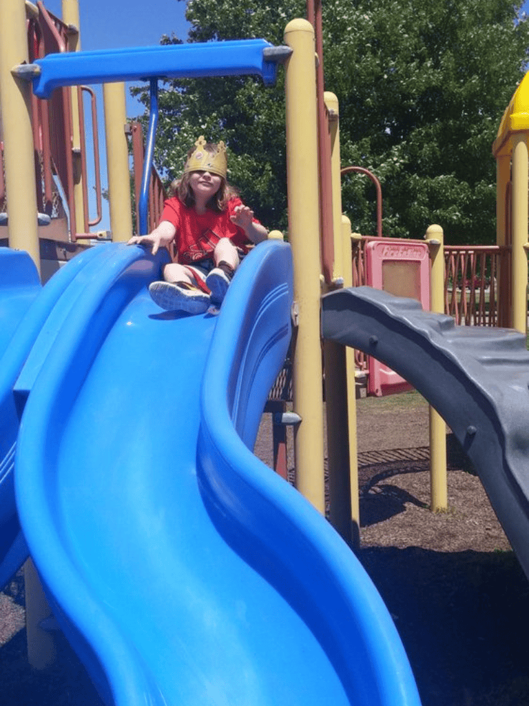 Child playing on colorful playground slide with crown, outdoor park fun, kids playground equipment.