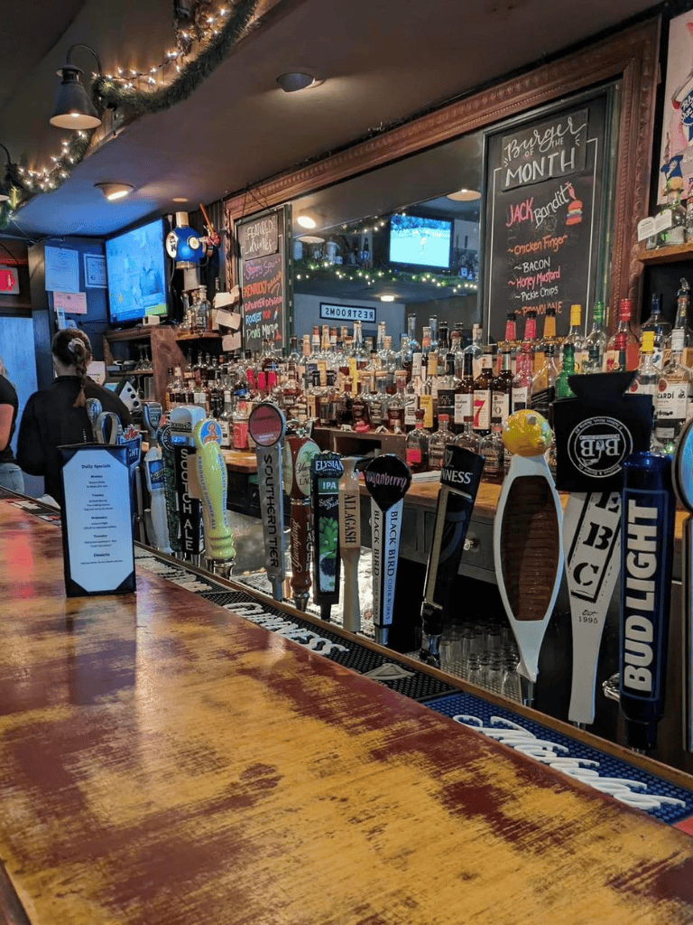 A10638A: A cozy bar with a variety of beer taps and a well-stocked liquor shelf in a lively pub setting.