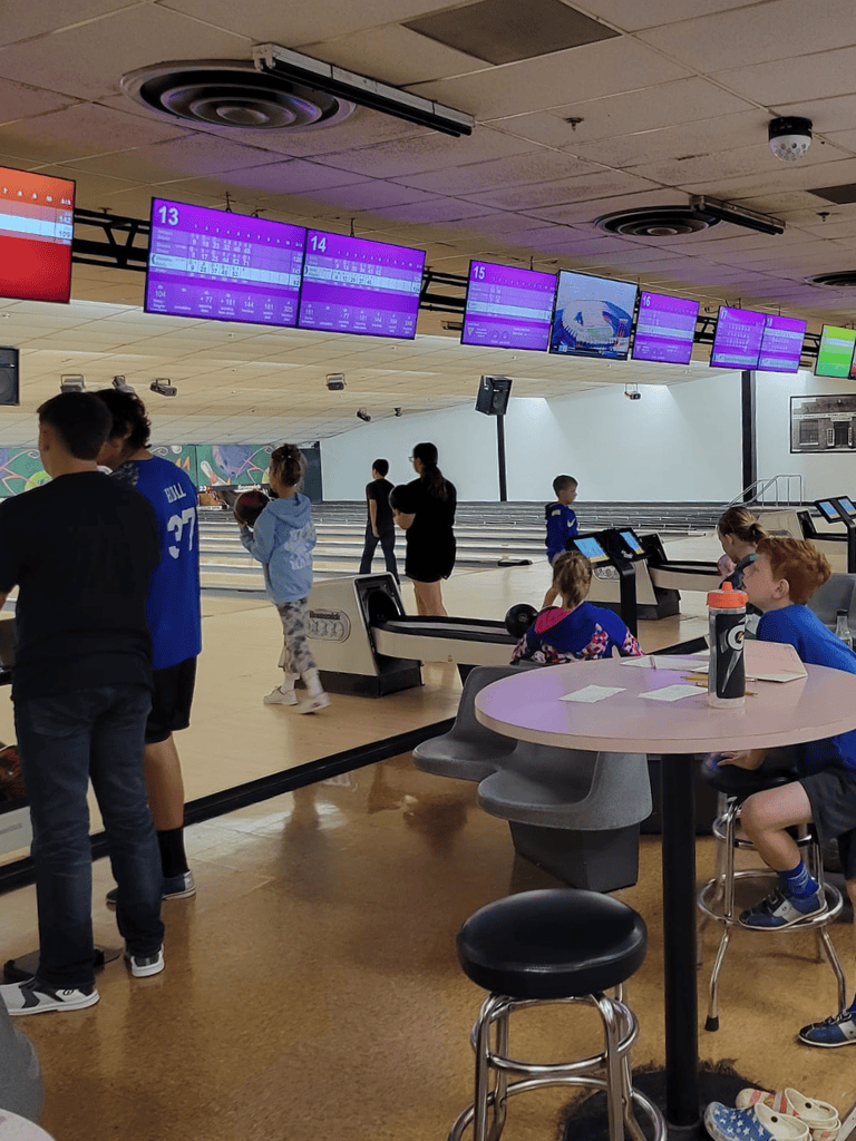 AlT: Modern bowling alley with digital score screens and group of children playing.