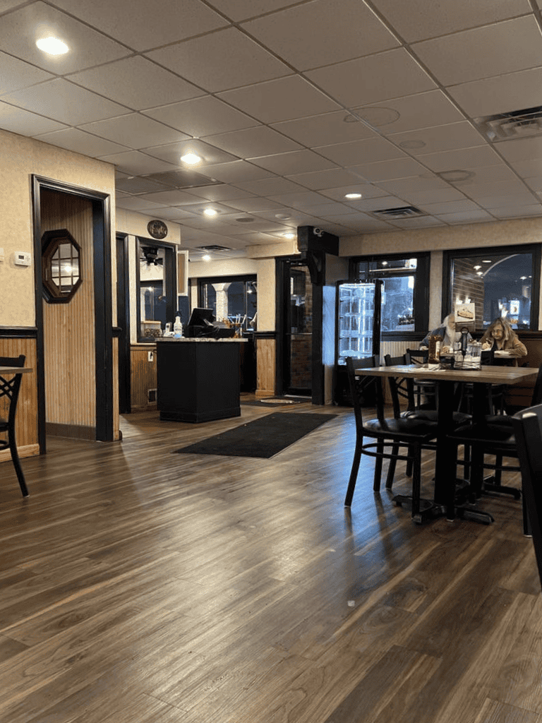 Cozy restaurant interior with wooden floors, black furniture, and customers dining, showcasing inviting ambiance.