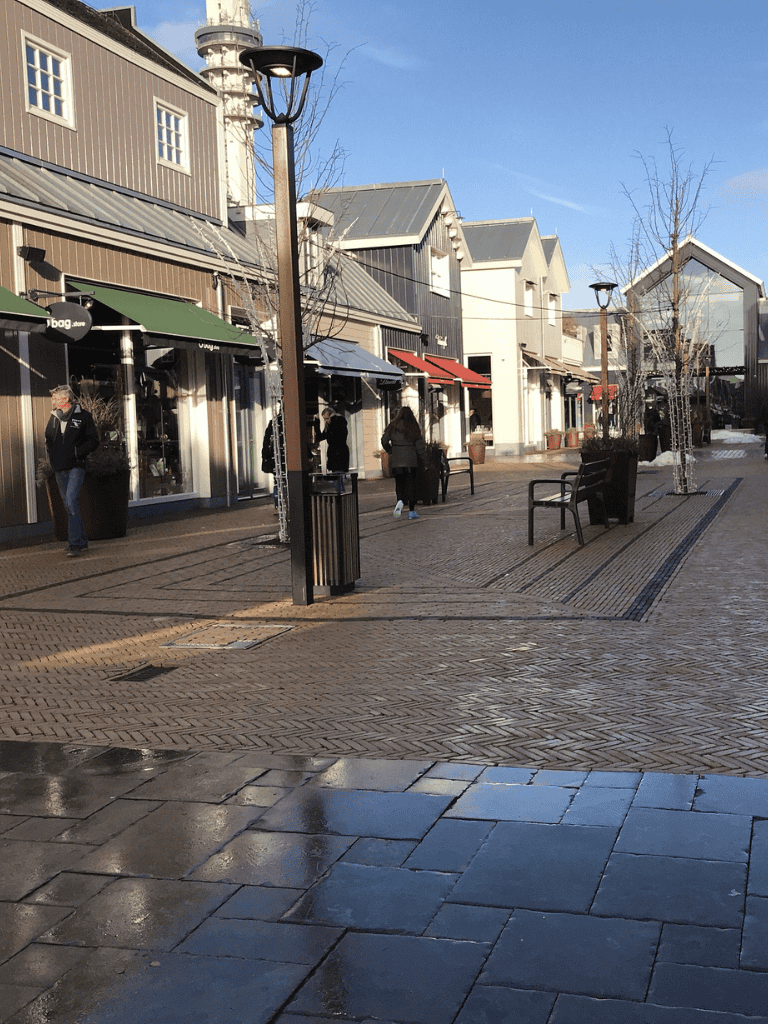 Outdoor shopping plaza with storefronts, benches, and trees, sunny winter day at QuestForDirections.