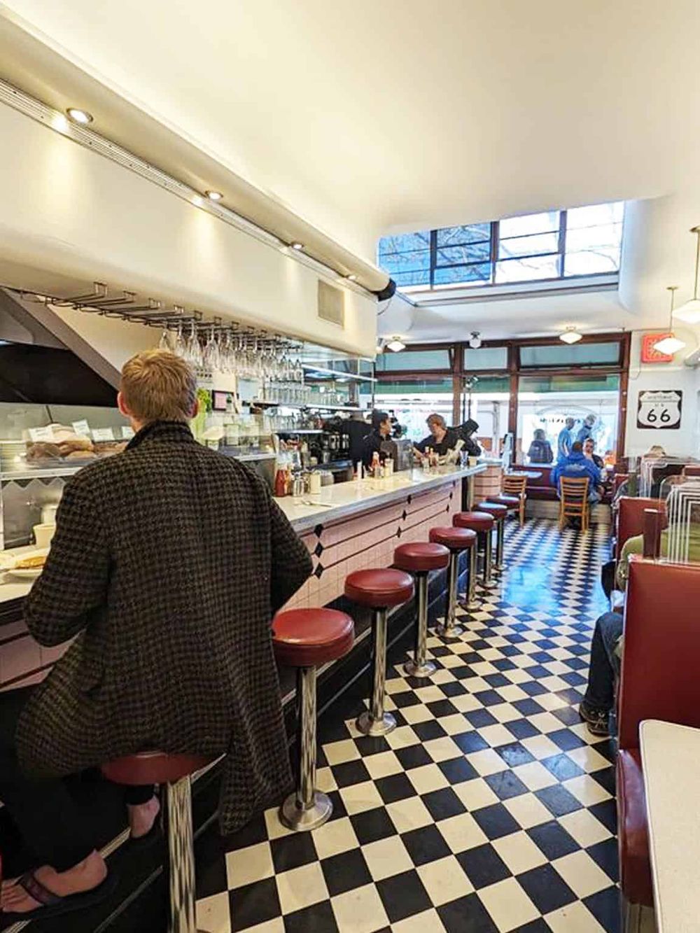 Cozy diner interior featuring a black-and-white checkered floor, bar seating, and customers enjoying breakfast.