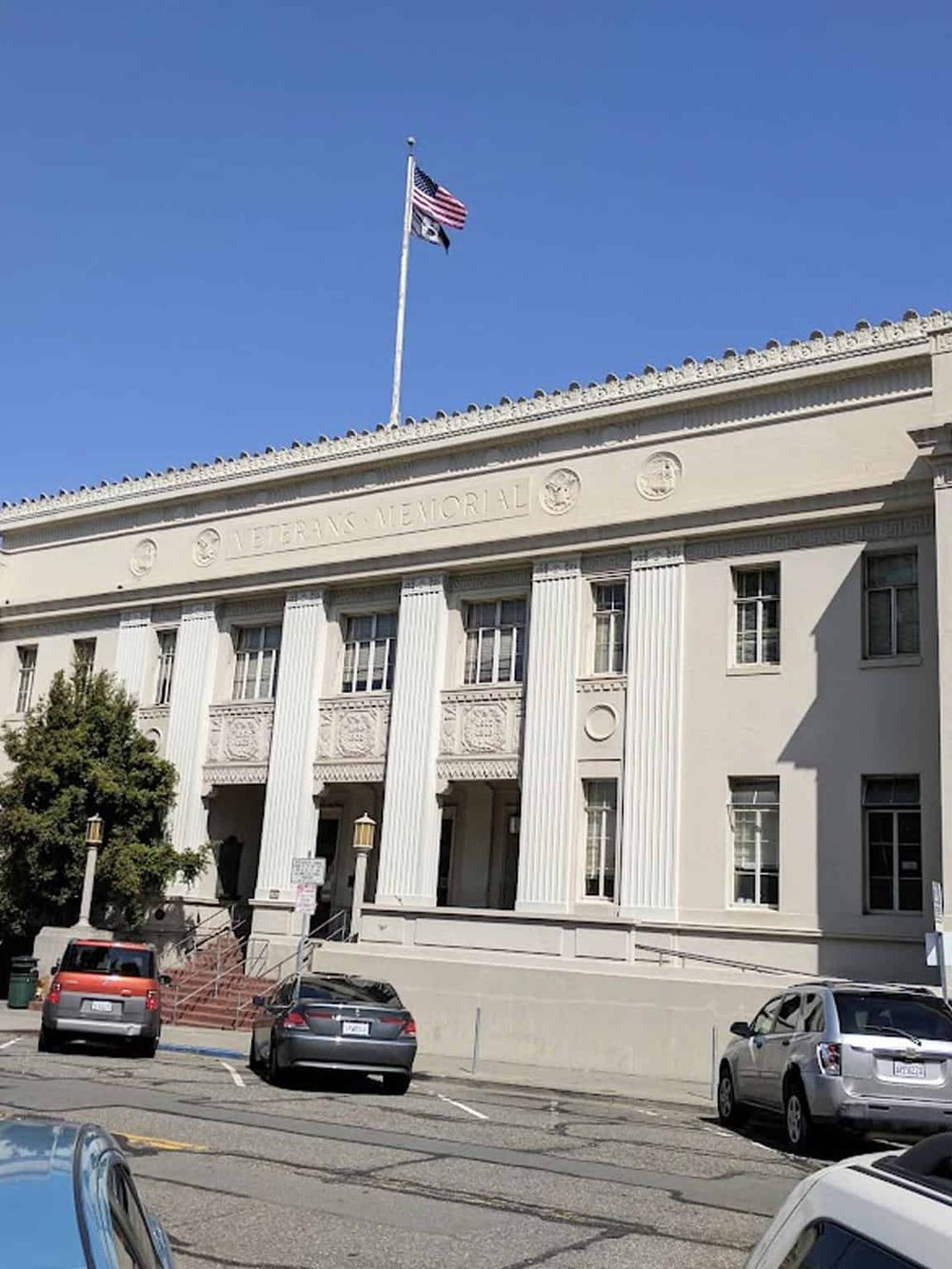 Historical veterans memorial building with American flags and parking lot, in a downtown area.
