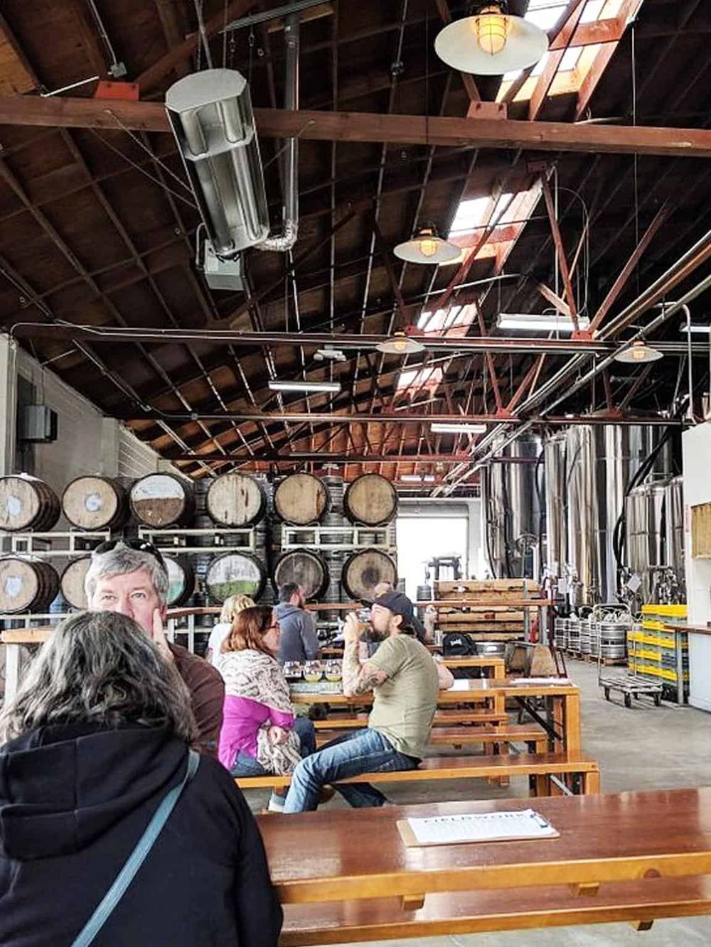Bright brewery interior with large wine barrels, industrial lighting, and casual seating area.