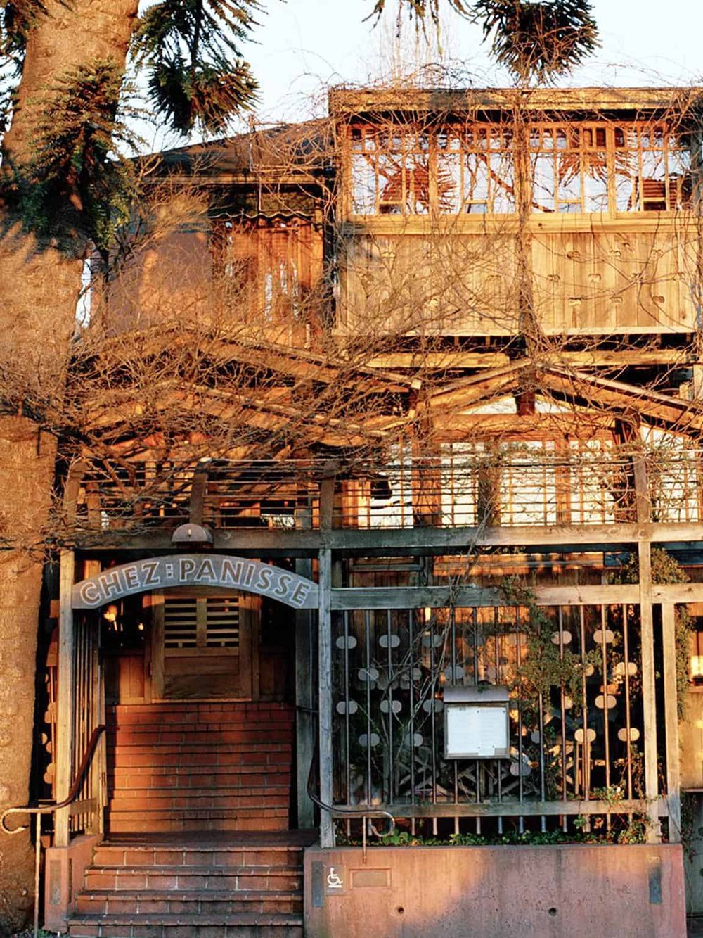 Weathered wooden house with a sign that reads "Chez Panisse" and bare trees in front.