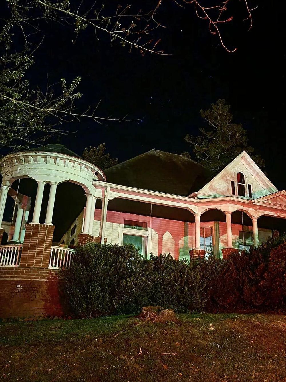 Spooky illuminated house at night with colonial architecture and starry sky in the background.