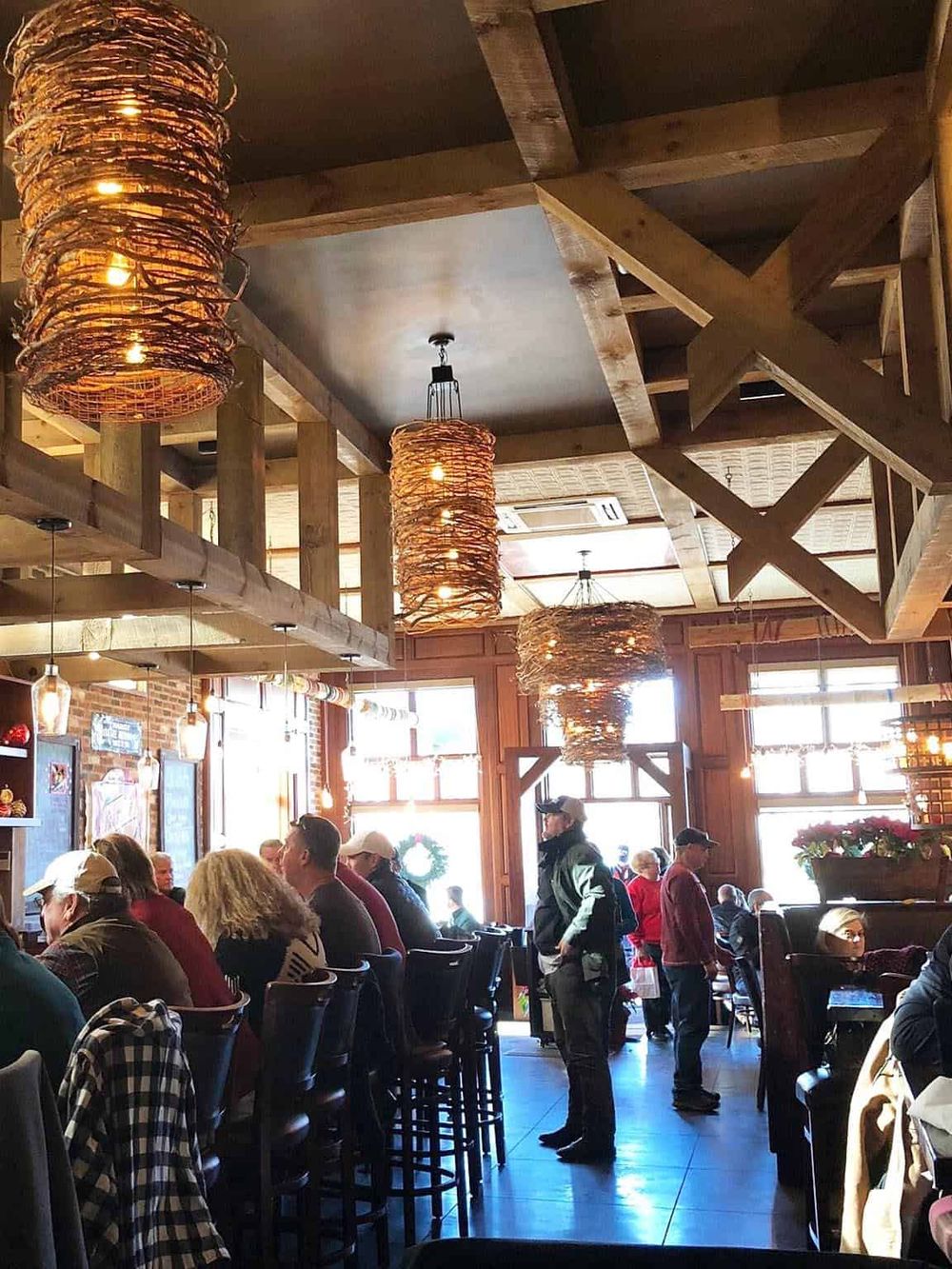 Warm inviting restaurant interior with rustic wood decor and hanging woven light fixtures, busy with customers dining and socializing.