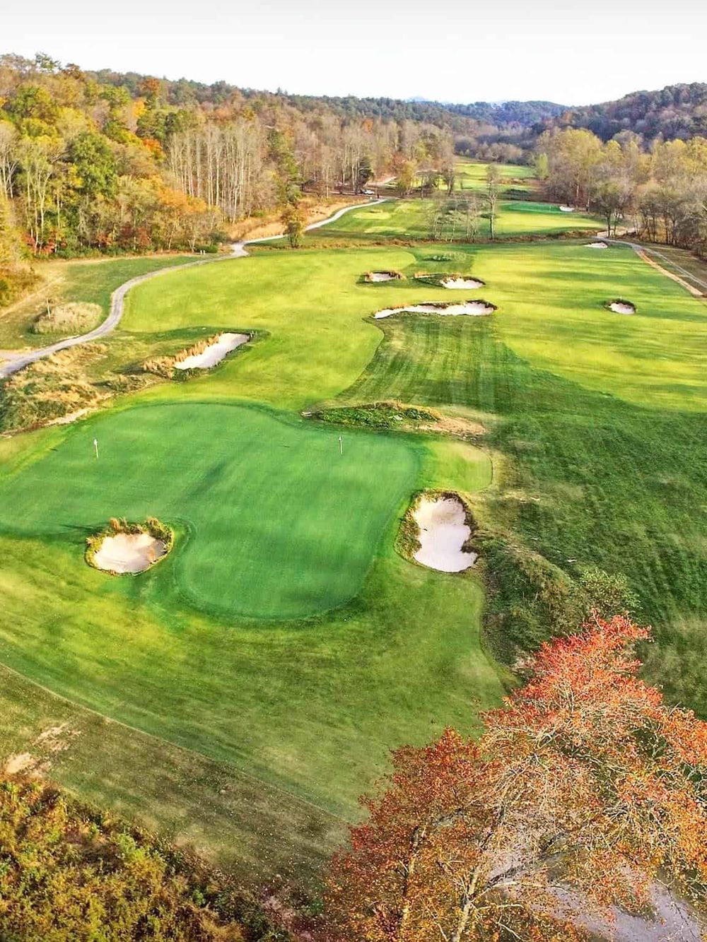 Lush golf course with sand traps and surrounding autumn foliage, scenic view for golf enthusiasts.