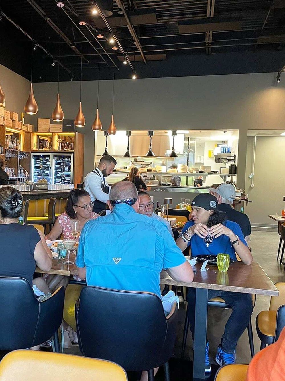 Modern restaurant interior with diners enjoying meals and open kitchen view, emphasizing dining experience and ambiance.