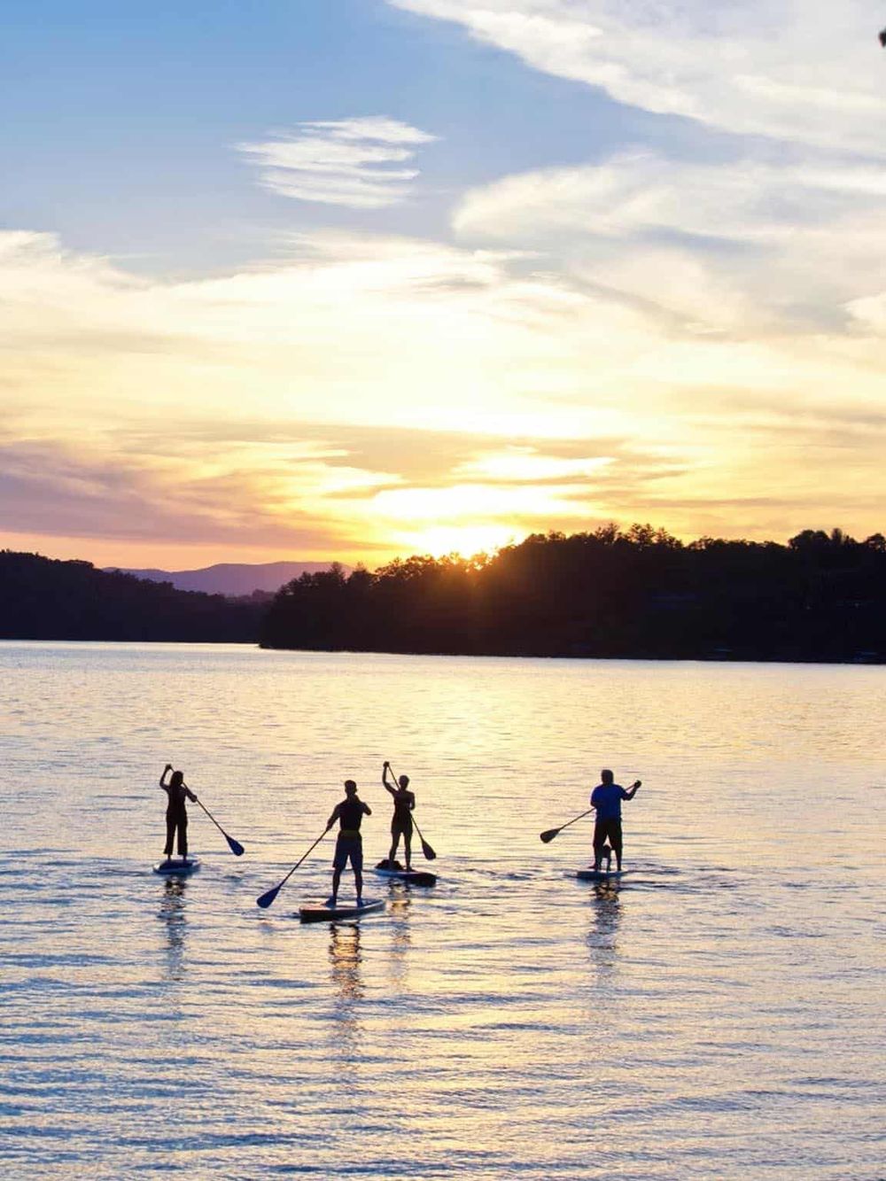 Paddleboarding at sunset on a calm lake with a scenic view and colorful sky.