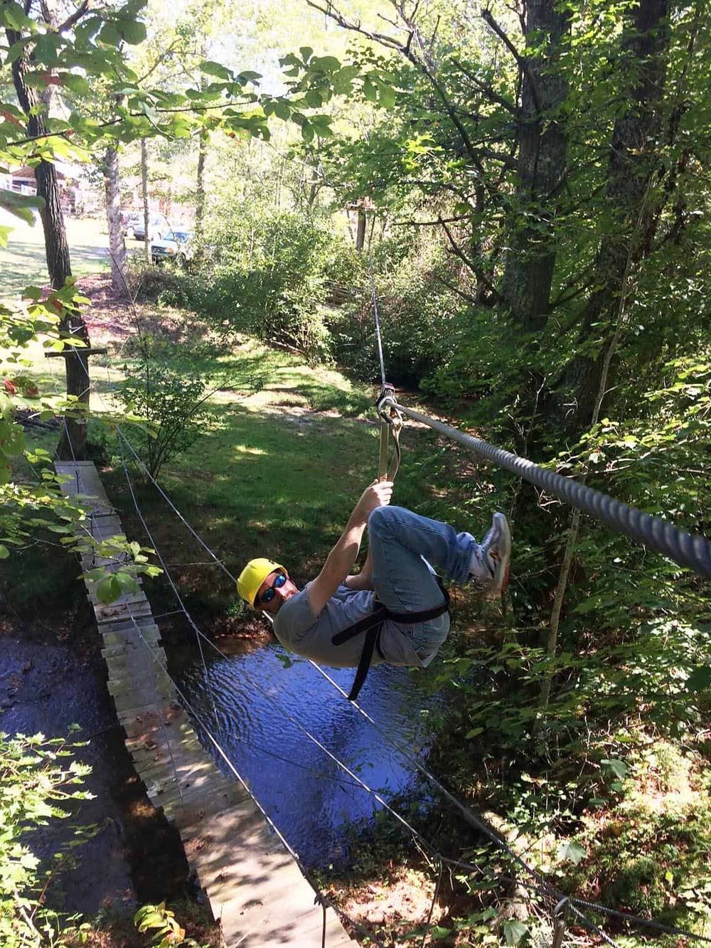 Thrilling zip line adventure through lush green trees over a small stream in a wooded park.