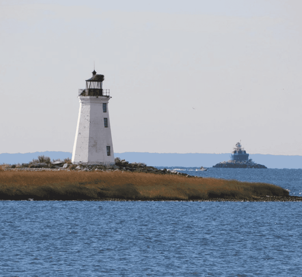 Lighthouse near water with distant ship, scenic coastal view for travel and navigation.