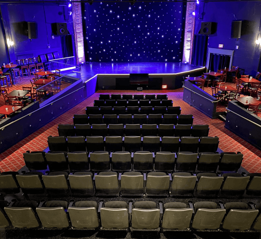 Artistic theater stage with seating for comedy shows and live performances, vibrant purple lighting, and cozy ambiance.