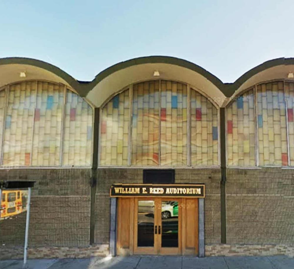 Colorful auditorium exterior with stained glass windows, entrance door, and William E. Reed Auditorium sign.