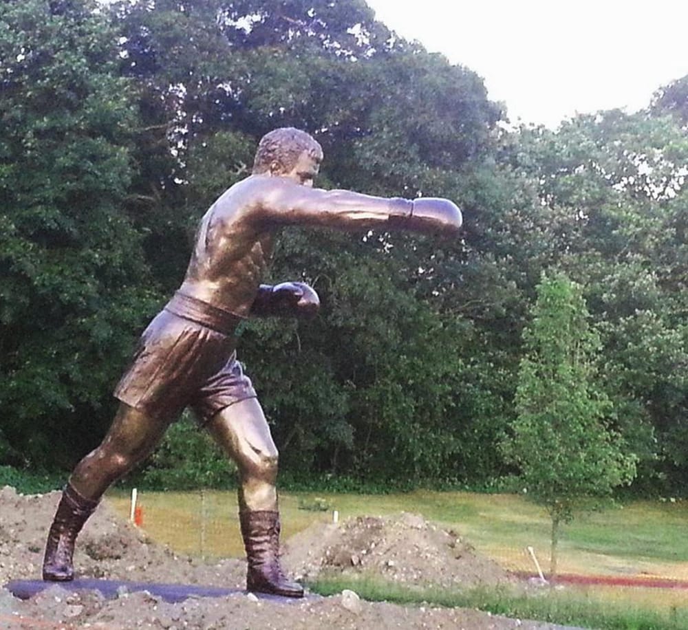 Bronze boxing statue outdoors, lifelike sports sculpture, athletic fighter in stance.