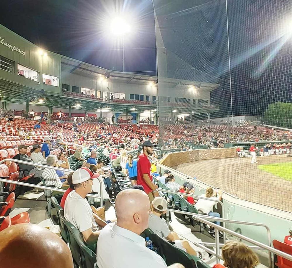 Night baseball stadium crowd enjoying a game at QuestForDirections. Fans seated in stadium seats under bright stadium lights.