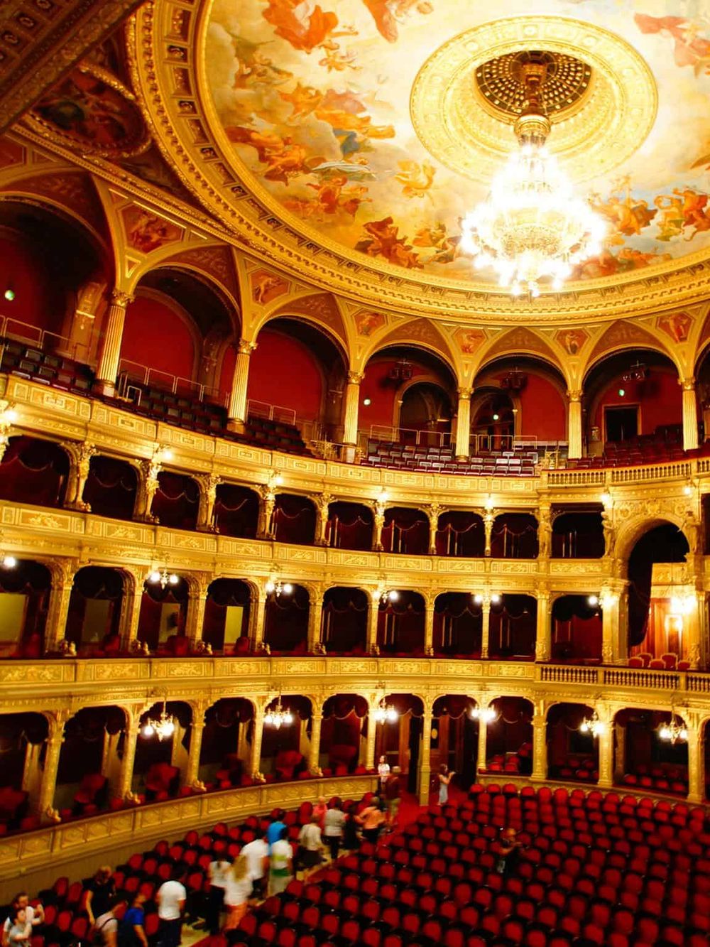 Elegant opera house interior with ornate gold balconies and a colorful ceiling fresco.