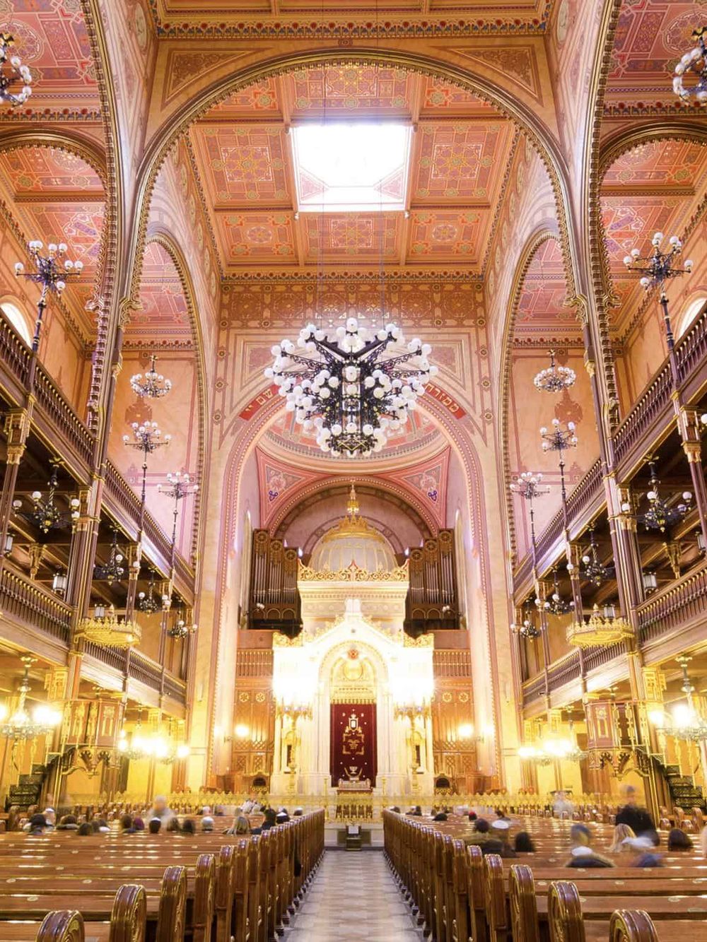 Intricate historic church interior with chandeliers, pink and gold accents, and ornate wooden details.