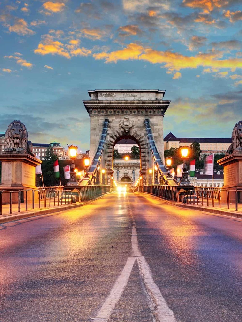 Sunset view of Chain Bridge in Budapest, Hungary, with illuminated lions and cityscape background.