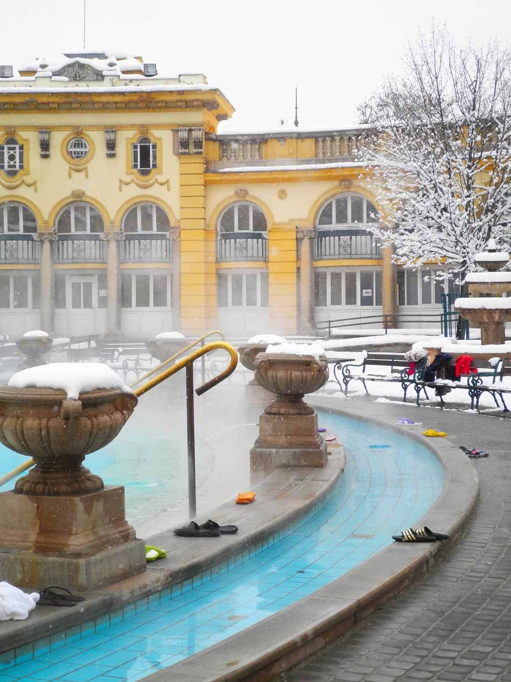 Snow-covered hotel with outdoor hot springs and steaming water, winter scene.