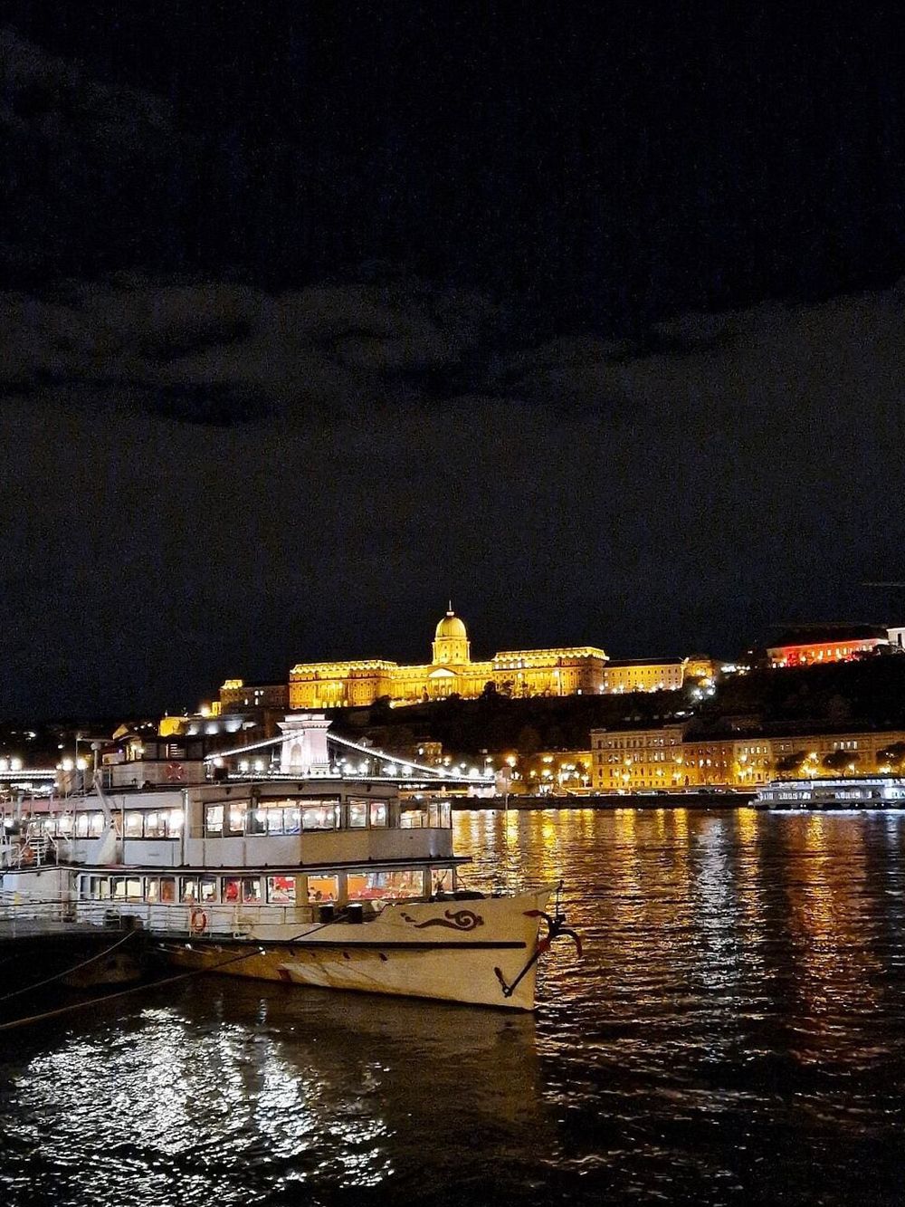 Stunning night view of a historic cityscape illuminated with a golden-domed building reflecting on the river.
