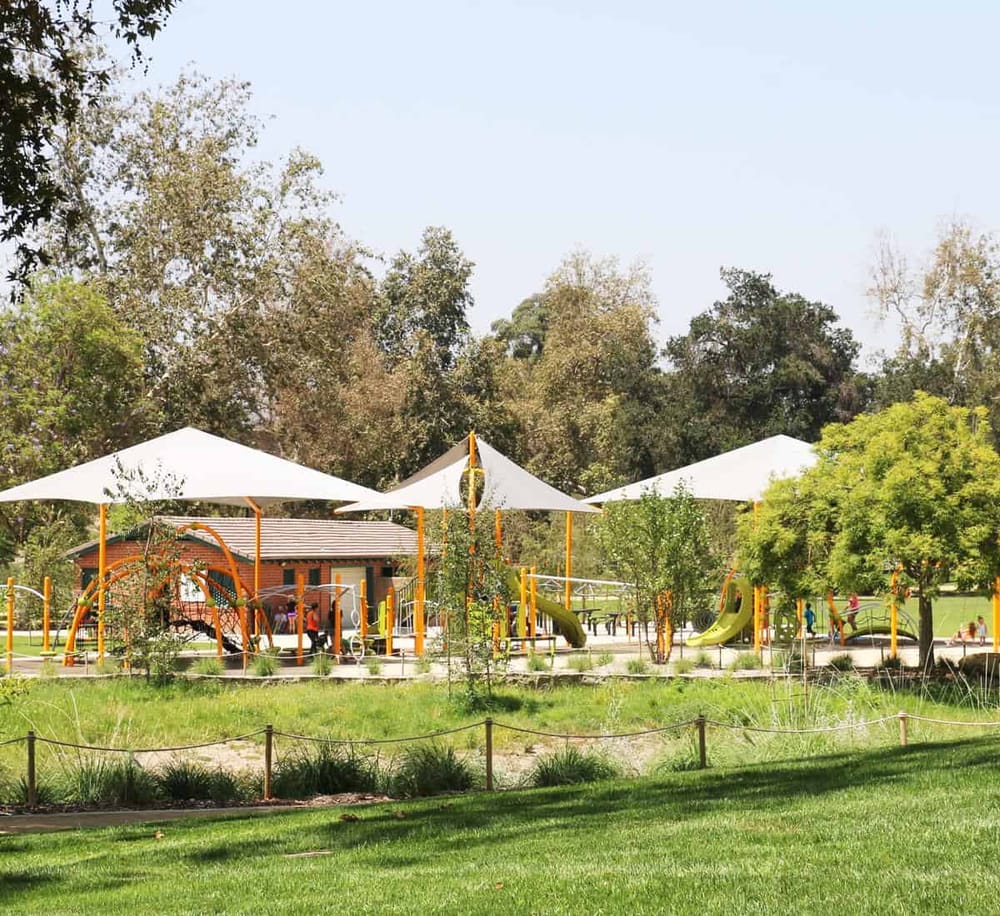 Colorful playground in a park with shade sails and lush greenery, ideal for family fun and outdoor recreation.