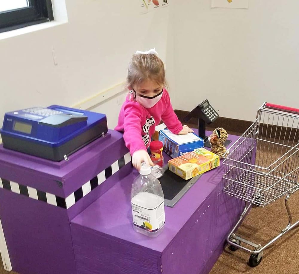 1. Child wearing mask shopping at checkout counter with shopping cart, groceries, and register.