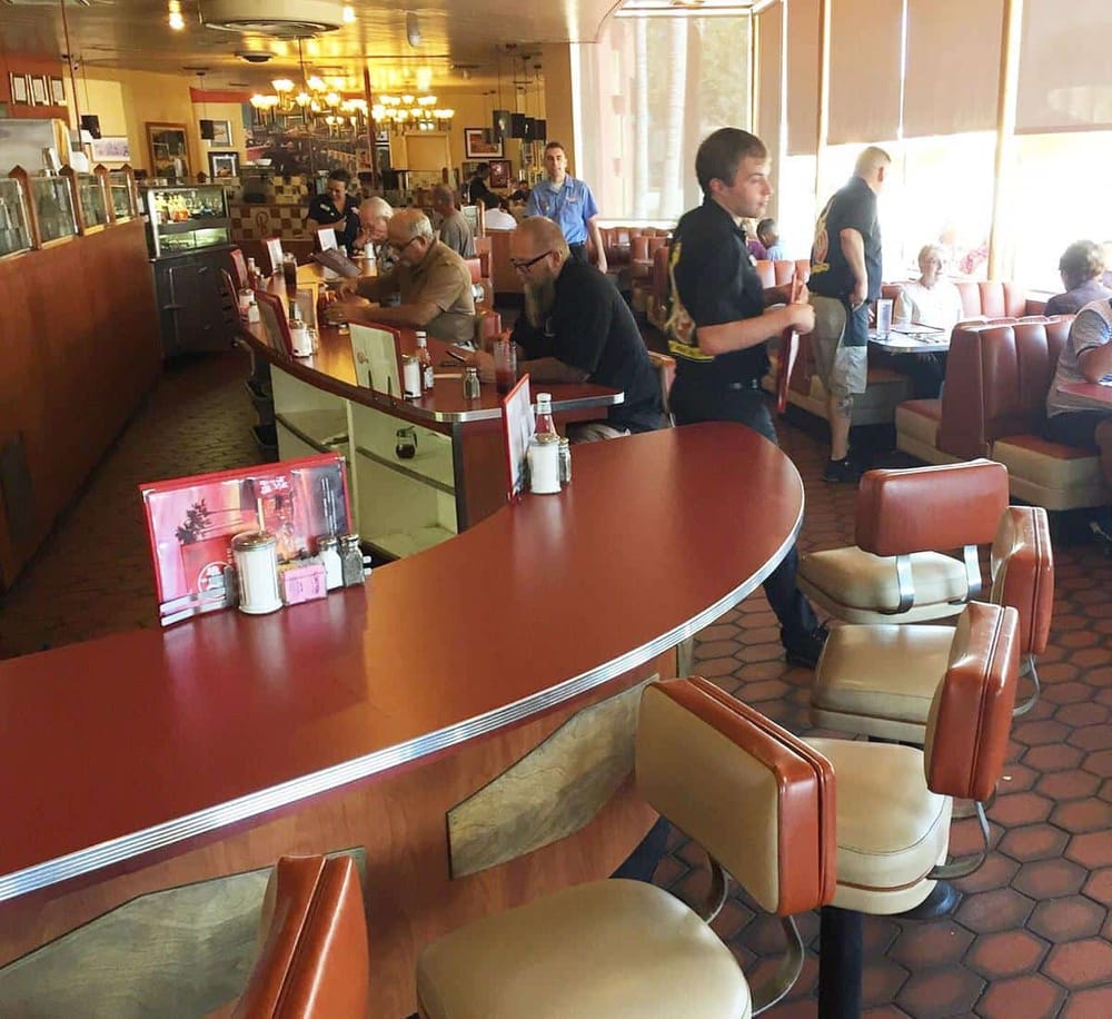 Seat dining restaurant with customers and waitstaff, retro decor, and sunlight through windows.