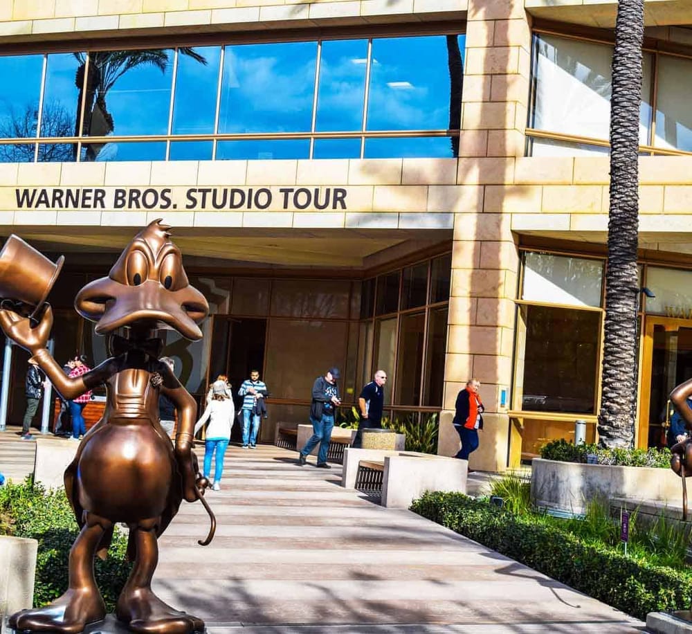 Colorful Warner Bros. studio tour building with iconic bronze cartoon character statue outside.
