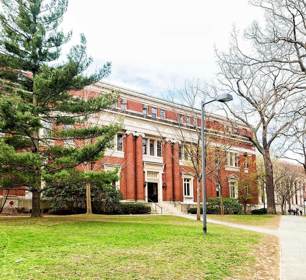 Historic brick university building with lush green trees and pathway, showcasing academic campus environment.