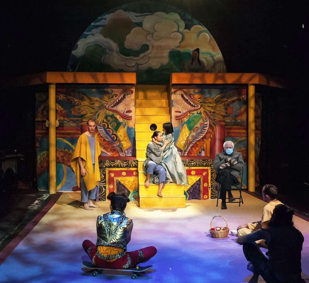 Vibrant Asian theatrical scene with actors performing on colorful set with dragons and clouds.