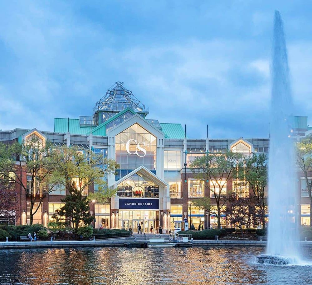 Modern shopping mall with water fountain, storefronts, and glass architecture in Cambridge, showcasing retail and entertainment facilities.