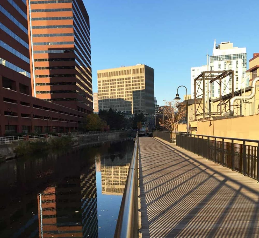 Bright cityscape with towering commercial buildings along a serene canal, emphasizing urban exploration and city navigation.