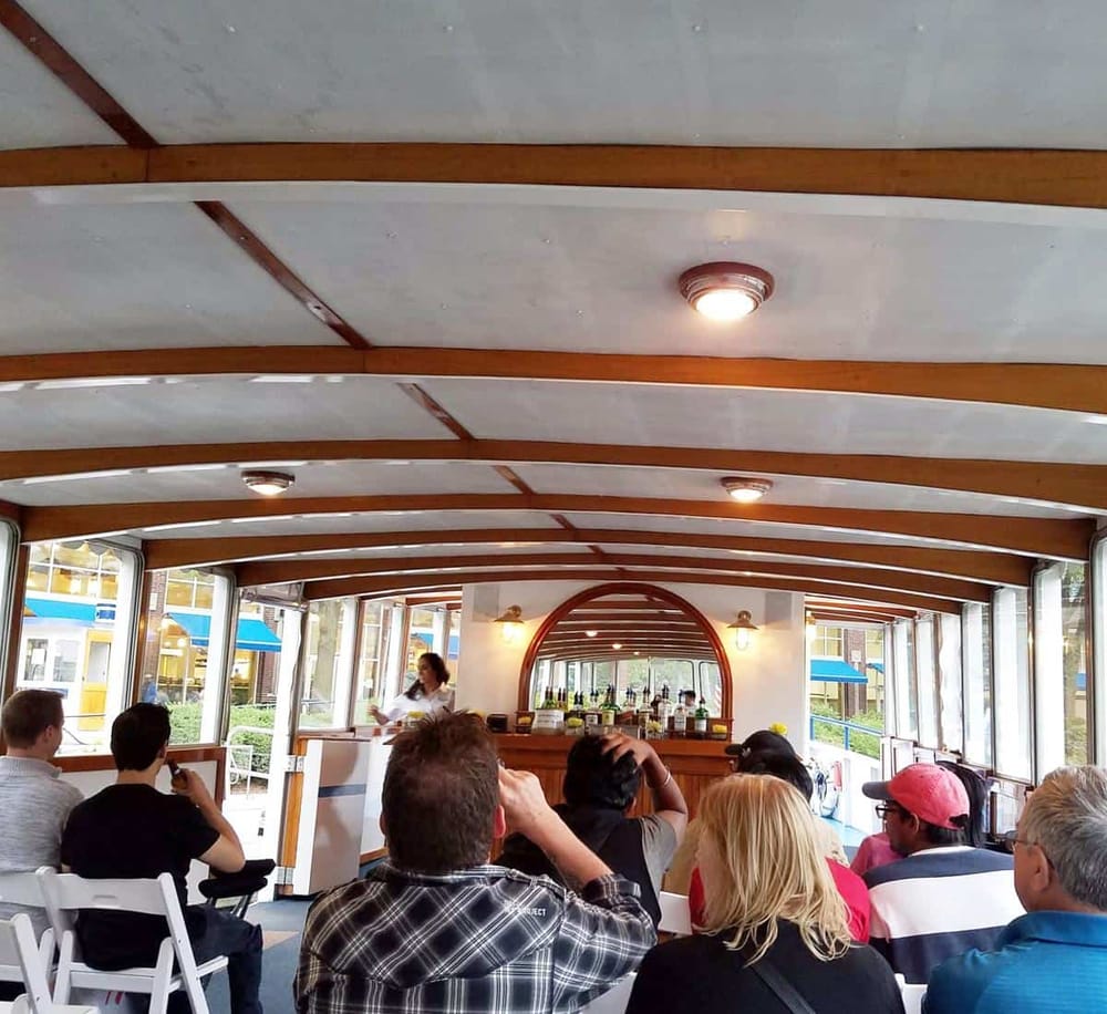 Bright indoor boat restaurant with large windows and group of people enjoying meal.