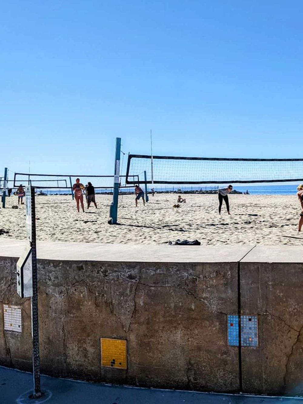 People playing volleyball on the sandy beach near the ocean, sunny day, outdoor sports, seaside recreation.