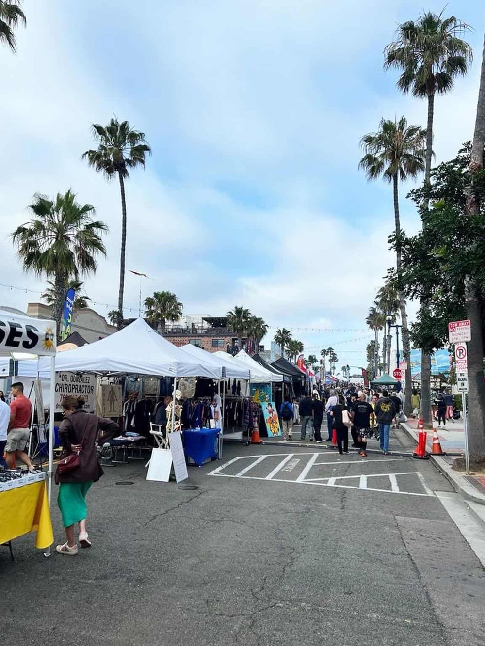 Colorful outdoor market in a sunny California street with palm trees and vendor tents.