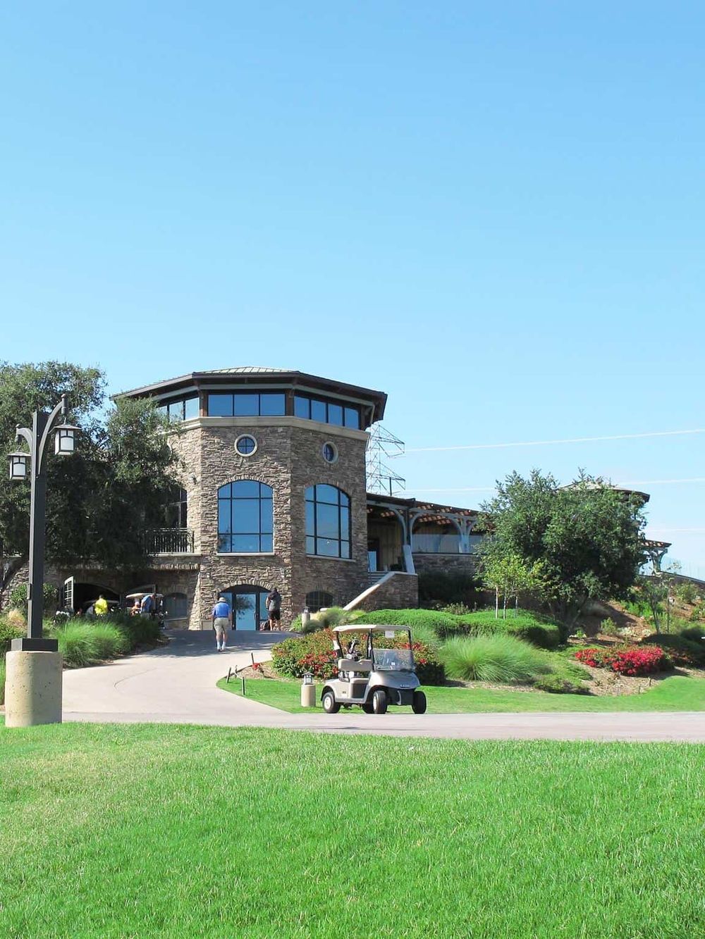 Elegant golf clubhouse with stone facade and large windows, surrounded by lush greens and a golf cart.