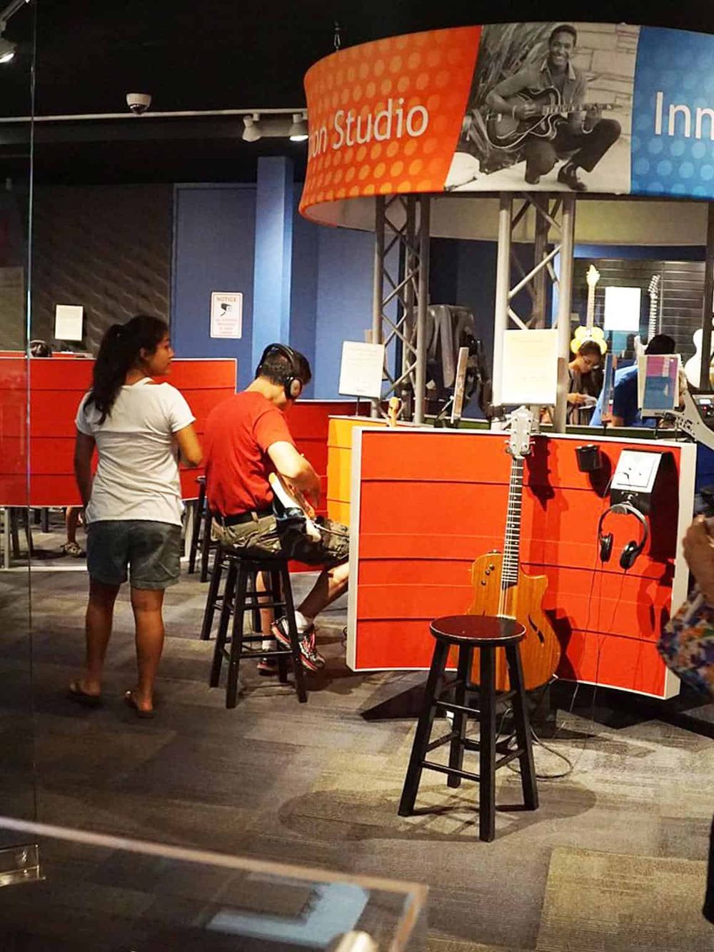 A vibrant music studio with students engaged in musical activities, featuring guitars and headphones for immersive learning.